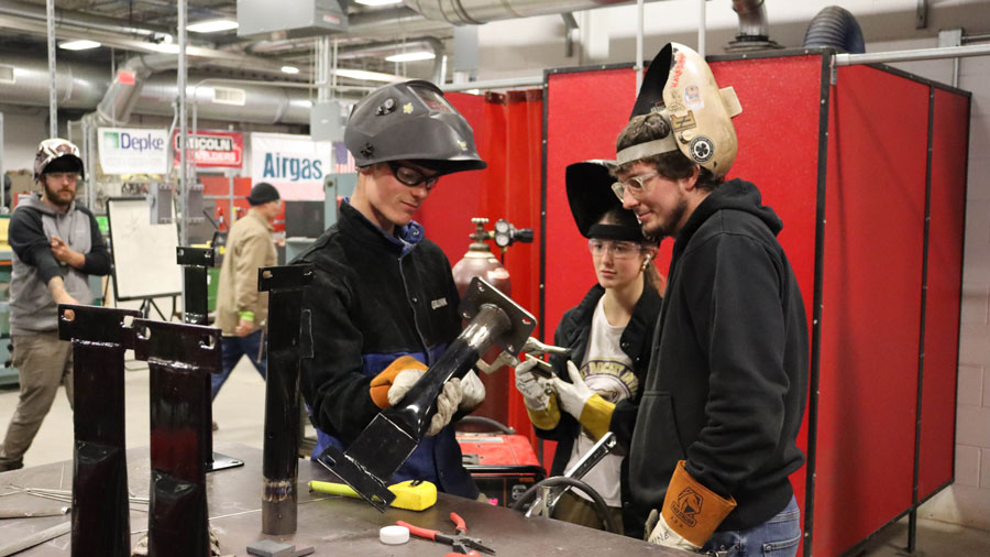 Three students in welding helmets inspecting a weld