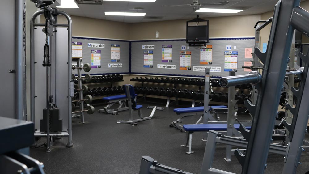 Various exercise equipment including benches, barbells, and a rack full of dumbbells